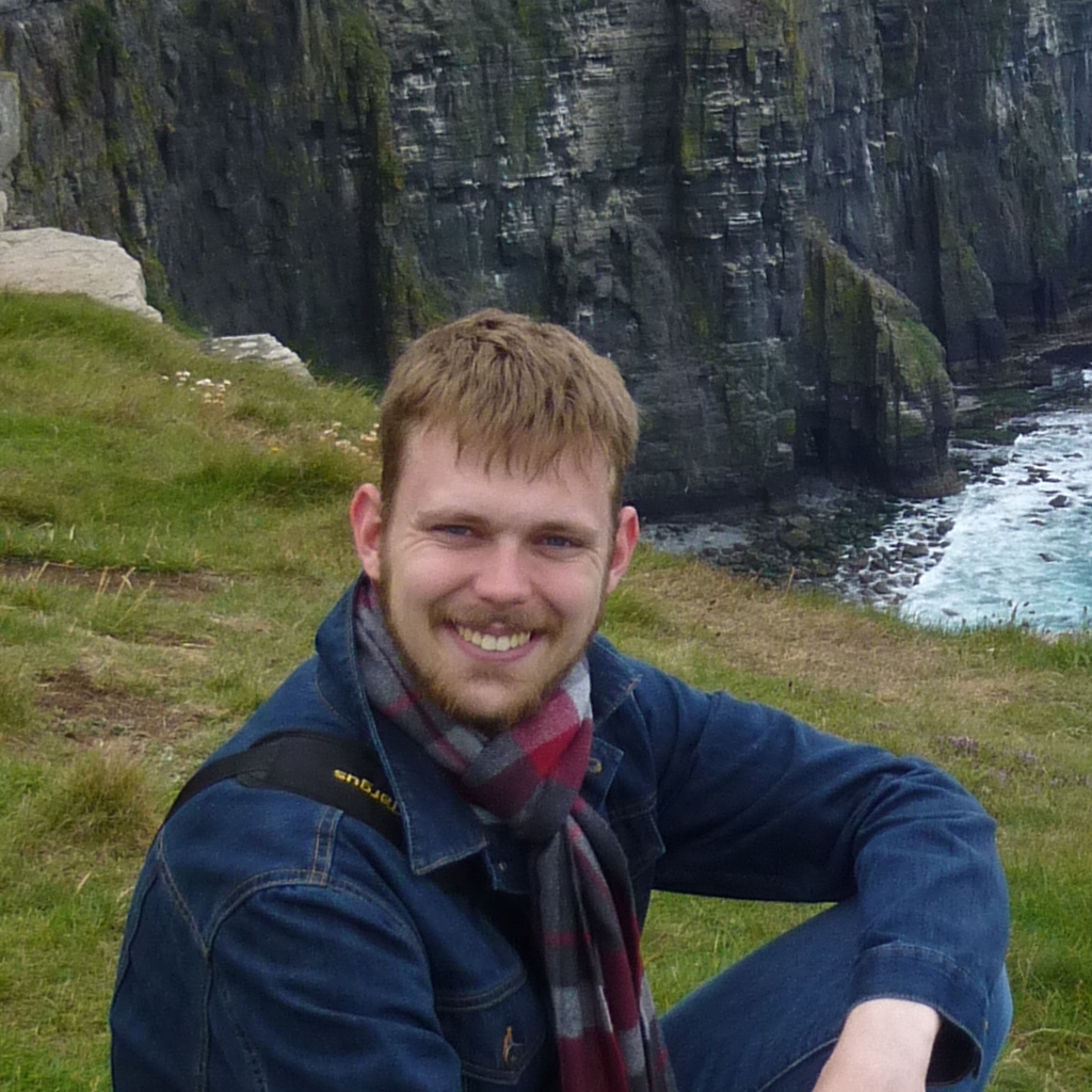 Profile photo of Ryan sitting in front of the Cliffs of Moher and smiling at the camera
